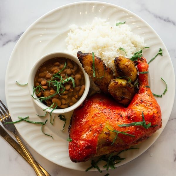 Lincoln Grill Cafe's roasted chicken leg with rice, beans, and plantains on a white plate.
