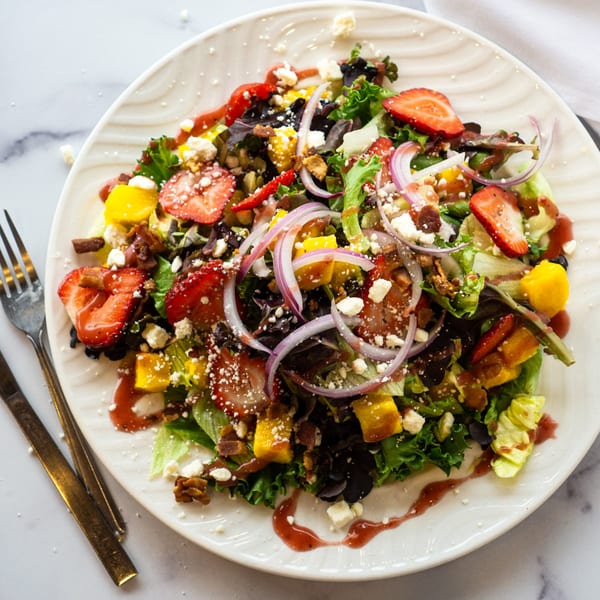 Colorful salad with strawberries, mango, red onion, feta, and nuts, drizzled with dressing.