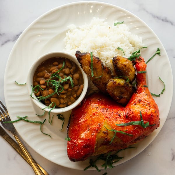 A plate of Lincoln Grill Cafe's roasted chicken, rice, beans, and plantains, garnished with herbs.