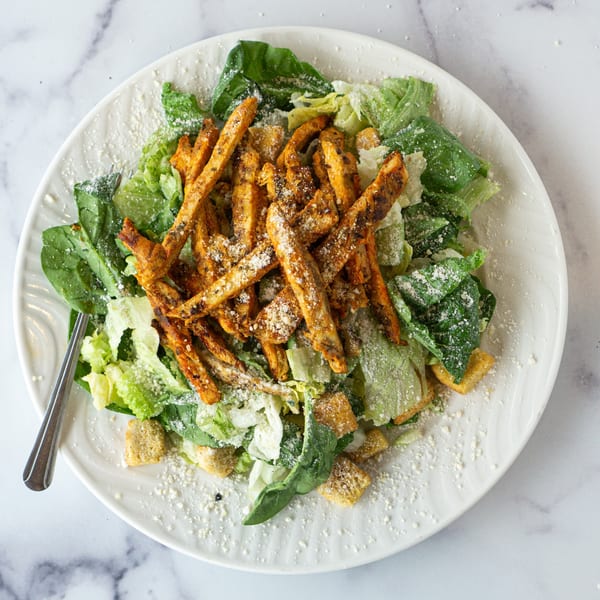 Caesar salad with grilled chicken strips, croutons, and parmesan cheese on a white plate.
