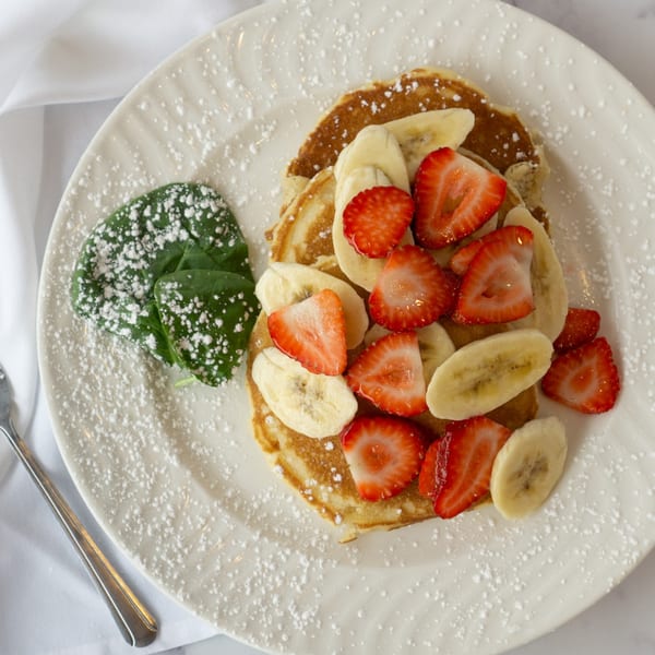 Pancakes topped with sliced strawberries and bananas, dusted with powdered sugar, on a white plate.