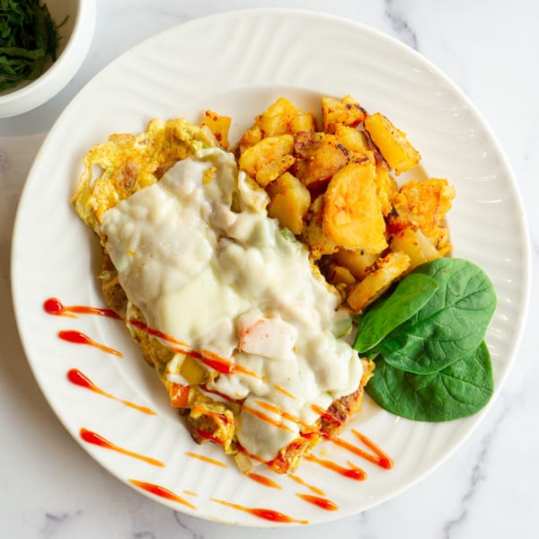 Lincoln Grill Cafe's omelet with melted cheese, home fries, spinach, and hot sauce drizzle.