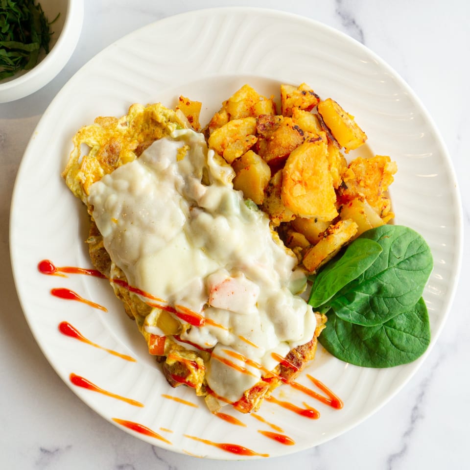 Lincoln Grill Cafe's omelet with melted cheese, home fries, spinach, and hot sauce drizzle.