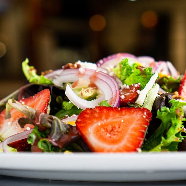 Close-up of a fresh salad with strawberries, red onions, and mixed greens on a white plate.