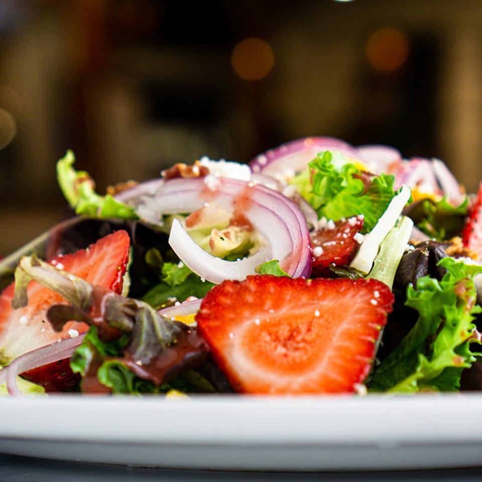 Close-up of a fresh salad with strawberries, red onions, and mixed greens on a white plate.
